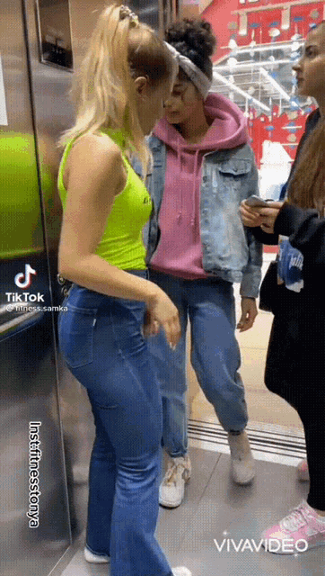 a woman in a neon green tank top is standing in an elevator next to a woman in a pink hoodie .
