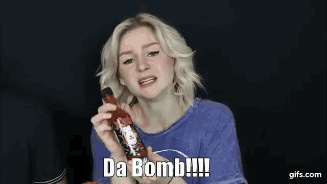 a woman in a blue shirt is holding a bottle of hot sauce and says da bomb !!!