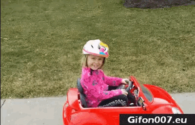 a little girl wearing a helmet is driving a red car