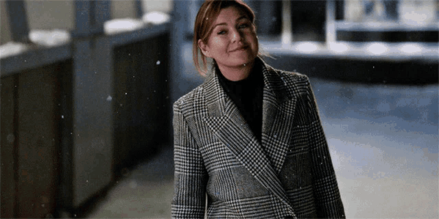 a woman wearing a plaid coat and black turtleneck is smiling
