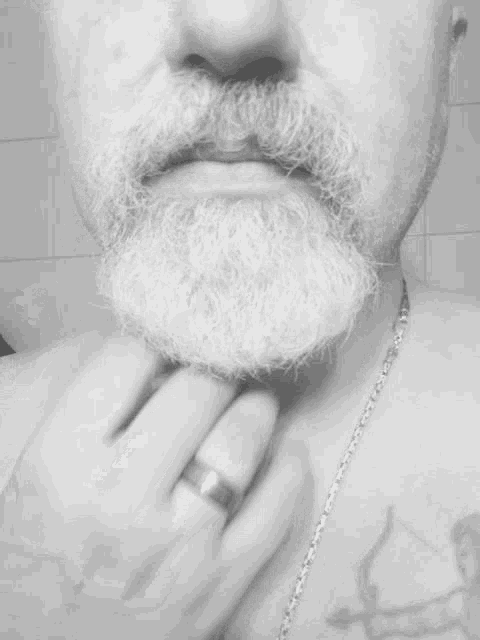 a man with a beard and a tattoo on his chest is touching his beard with his hand .