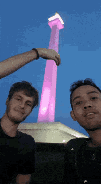two men are posing in front of a pink tower