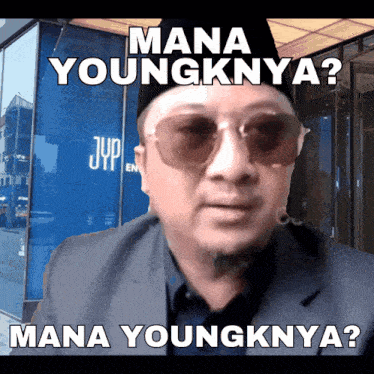 a man wearing sunglasses stands in front of a building that says jyp on it