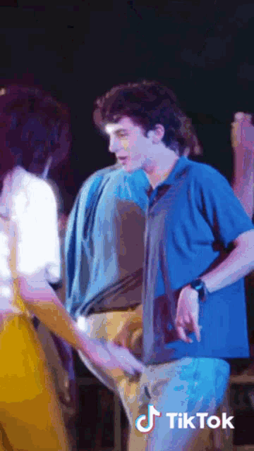 a man in a blue shirt is holding a woman 's hand and a tiktok logo can be seen behind him
