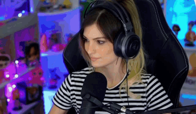 a woman wearing headphones and a striped shirt is sitting in a chair with a microphone