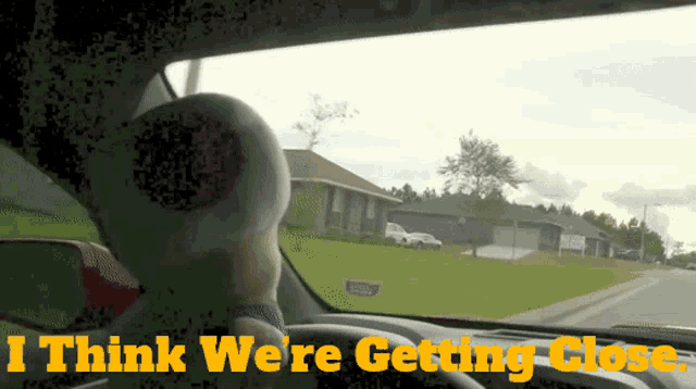 a person driving a car with the words " i think we 're getting close " on the dashboard