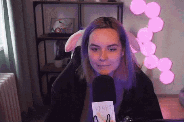 a woman with purple hair is sitting in front of a microphone with a card that says papaya