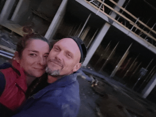 a man and woman pose for a picture in front of a building under construction