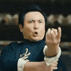 a man in a blue shirt is making a funny face while holding his fist up in the air .