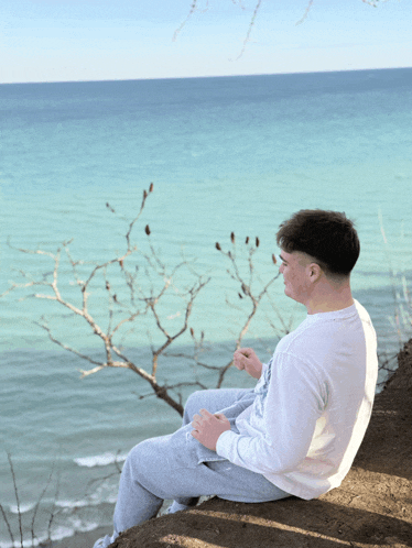 a young man sitting on a rock overlooking the ocean