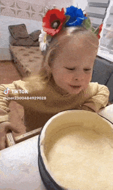 a little girl wearing a flower crown is looking at a bowl of food