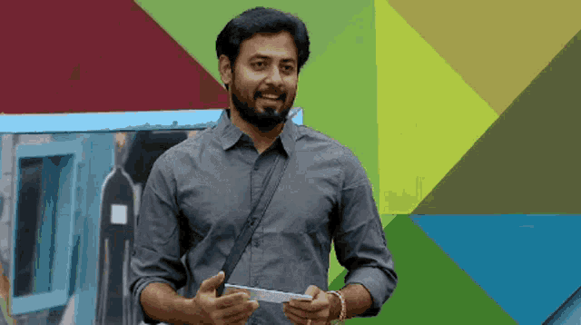 a man with a beard is standing in front of a colorful wall holding a piece of paper
