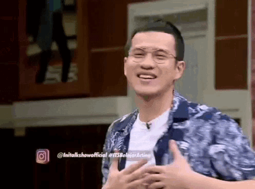 a man wearing glasses and a blue shirt is smiling with his hands on his chest