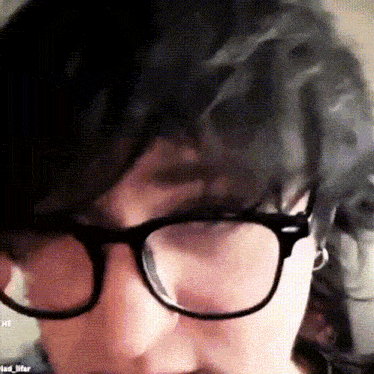 a close up of a person wearing glasses with the word he on the bottom left