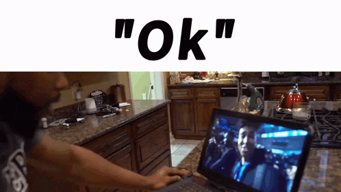a man is using a laptop in a kitchen and the word ok is above him