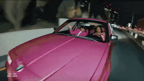 two women are driving a pink car with the dor brothers on the hood