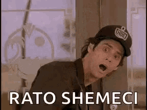 a man wearing a baseball cap is standing in front of a window with his mouth open and says rato shemeci .