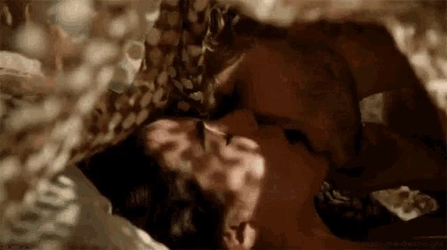 a man and woman are kissing under a blanket in bed .