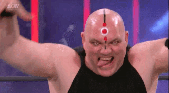 a bald man with a red circle on his forehead is making a funny face with his tongue out
