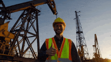 a man wearing a hard hat and safety vest is giving a thumbs up sign