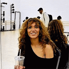 a woman with curly hair is sitting in front of a mirror holding a drink and smiling