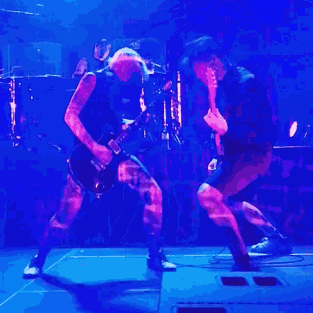 a man is playing a guitar while another man sings into a microphone on a stage