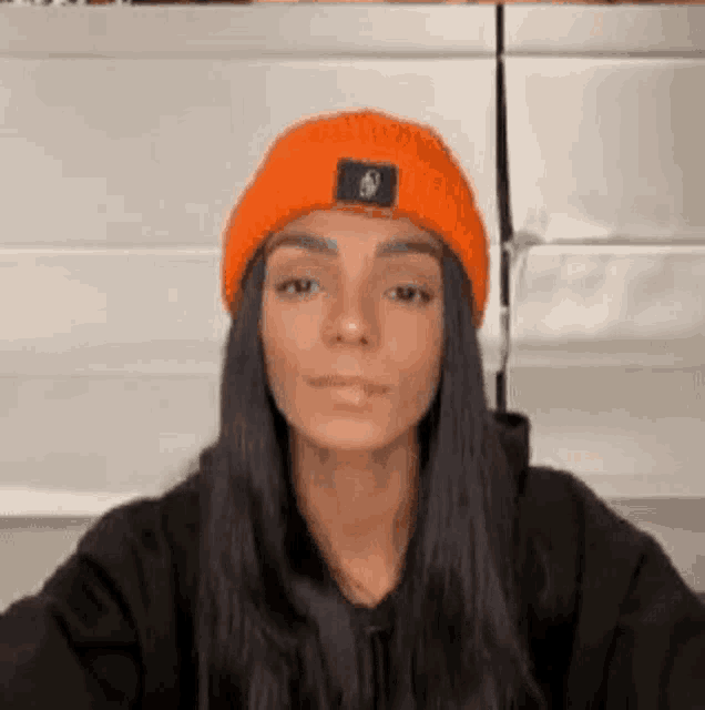 a woman wearing a black hoodie and an orange beanie is making a funny face .
