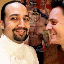 two men are posing for a picture in front of a collage of men 's faces