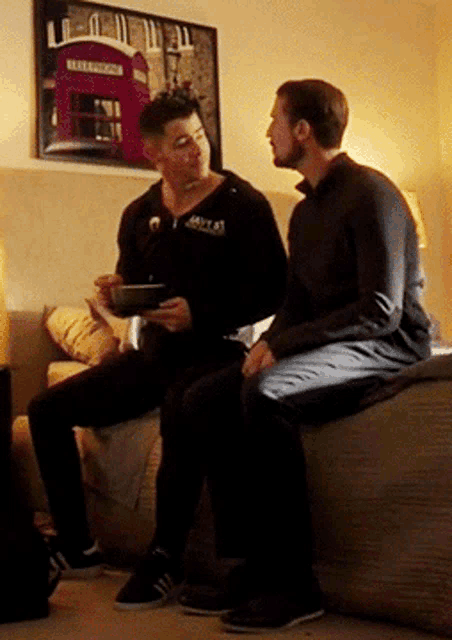 two men are sitting on a couch with a picture of a red telephone booth on the wall behind them