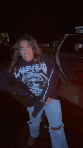 a woman wearing a black shirt with a skull on it is dancing in the dark
