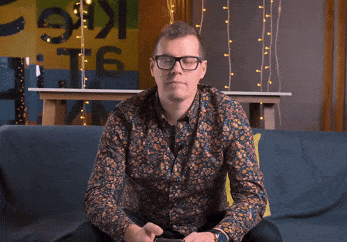 a man wearing glasses is sitting on a blue couch looking at his phone