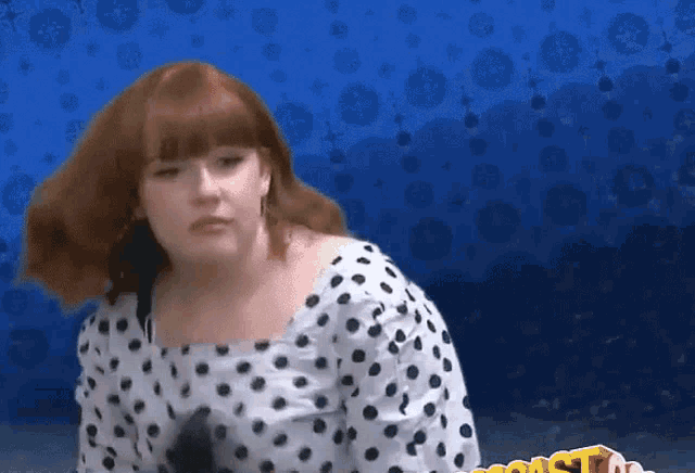 a woman in a white and black polka dot top stands in front of a blue background with the word coast on it