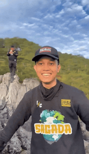 a man wearing a sagada shirt stands on a rocky cliff