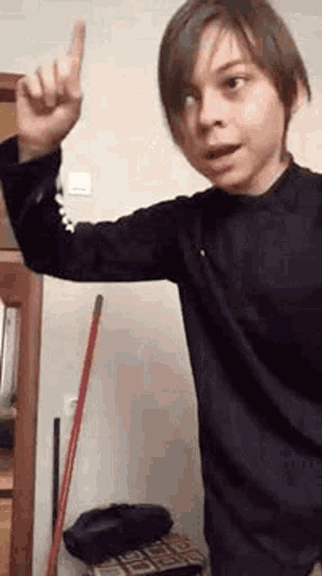 a young boy is pointing up with his finger while standing in front of a mop .