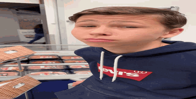 a boy wearing a blue levi 's sweatshirt stands in front of a display case of meat