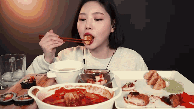 a woman is eating food with chopsticks at a table with a measuring cup in the background