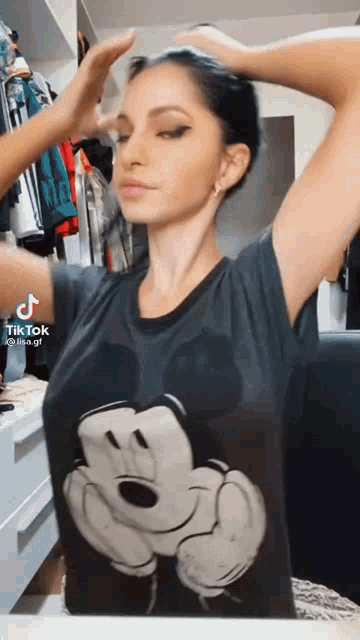 a woman wearing a mickey mouse t-shirt adjusts her hair .
