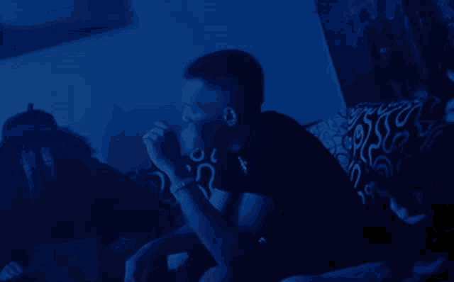 a man is smoking a cigarette in a dark room with a blue light behind him