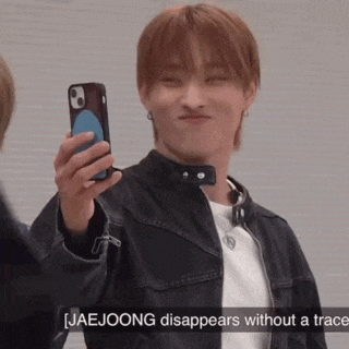 a young man in a leather jacket is holding a cell phone and making a face