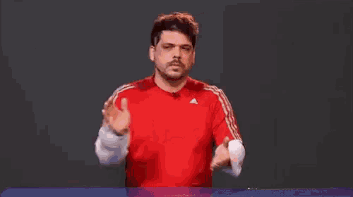 a man in a red shirt is clapping his hands in front of a black background .