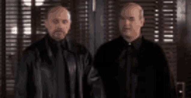 two men in black jackets and ties are standing next to each other in a room .