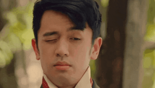 a young man in a suit and tie is making a funny face with his eyes closed .