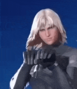 a man with long blonde hair is wearing a black suit and gloves and is standing in front of a blue background .