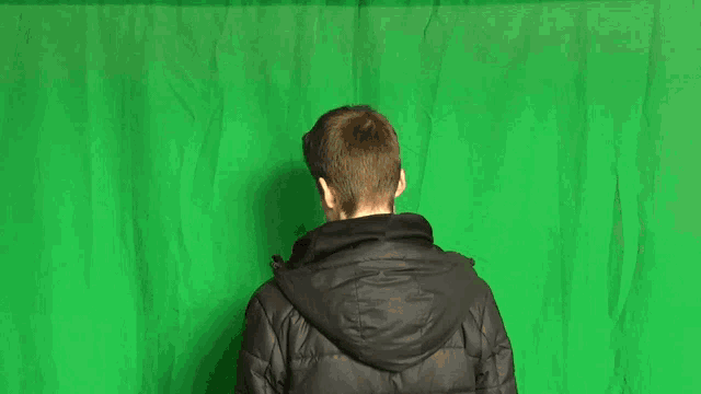 a young man wearing a nike jacket stands in front of a green screen