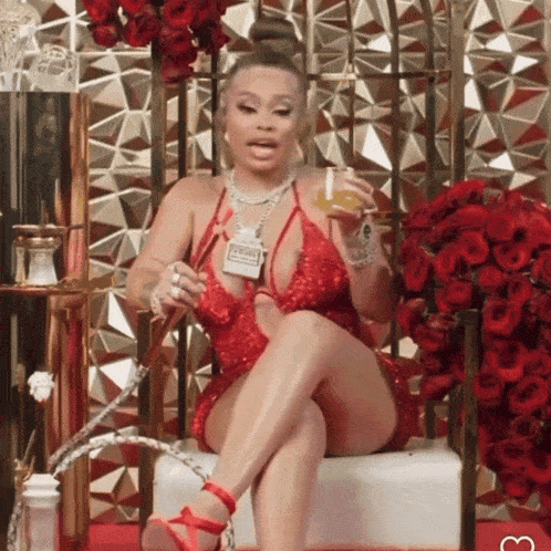 a woman in a red dress is sitting in a chair holding a bottle of perfume