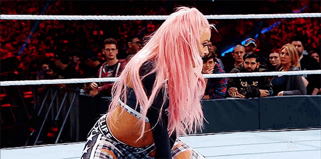 a woman with pink hair is kneeling in a wrestling ring