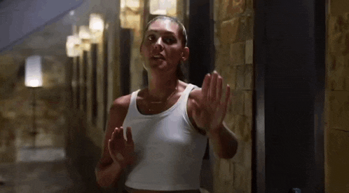 a woman in a white tank top is walking down a hallway .