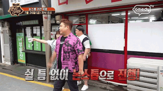 a man in a purple shirt is standing in front of a store that says comedy on it