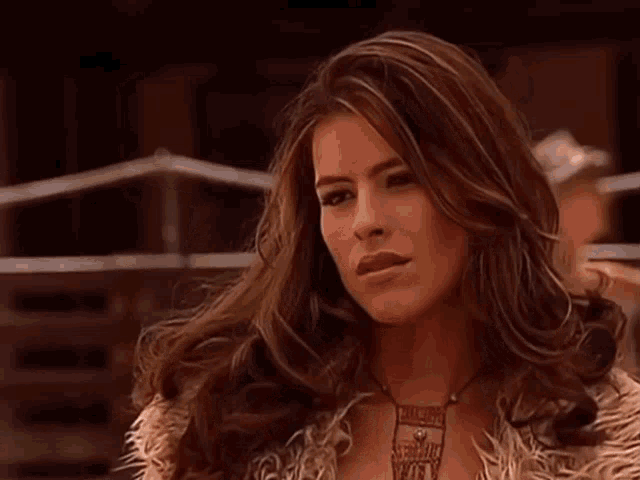 a woman with long brown hair is wearing a fur coat and necklace .