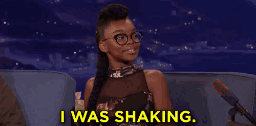 a woman with glasses is sitting in front of a microphone and saying i was shaking .